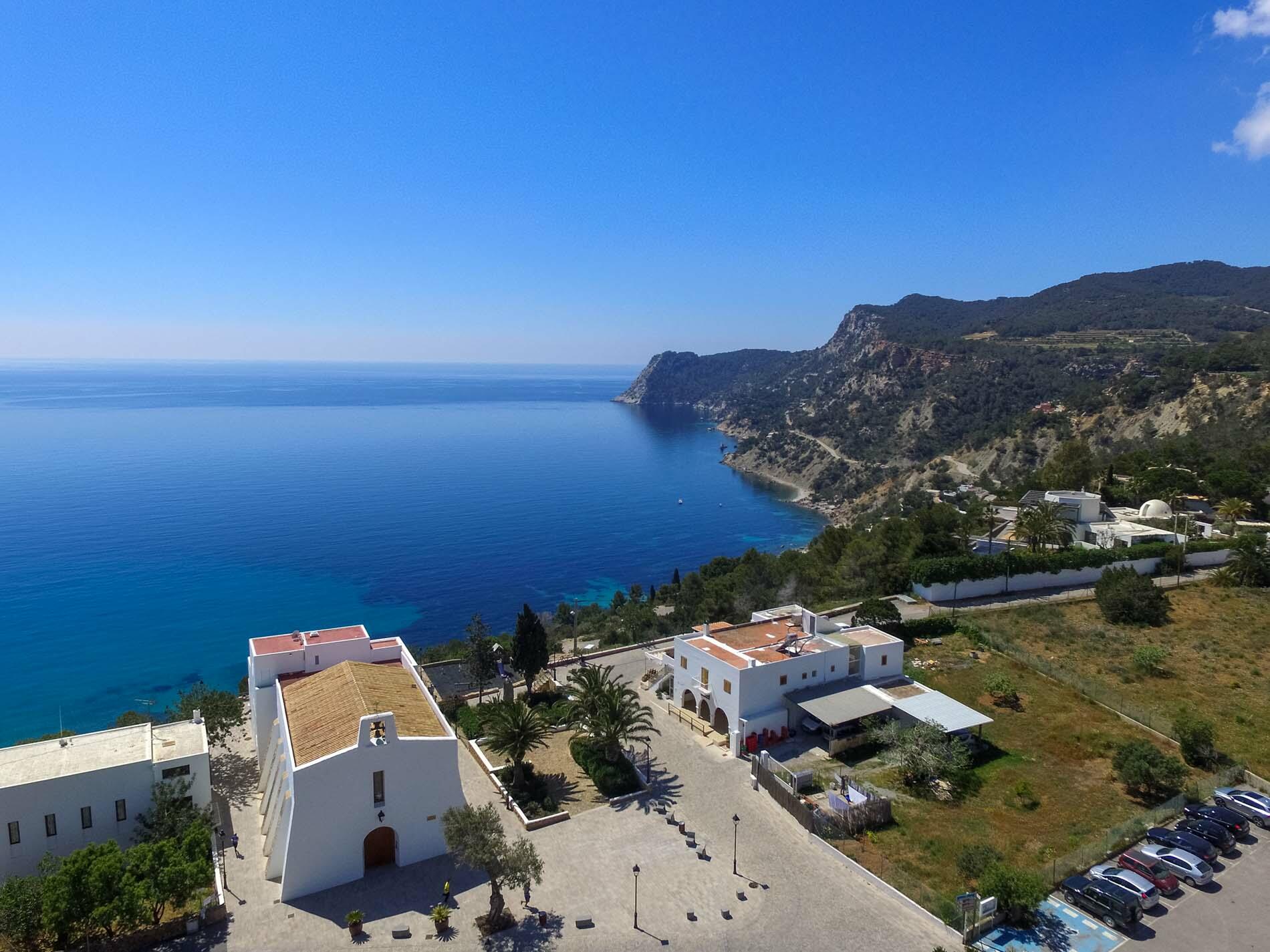 Vista elevata di Es Cubells, Ibiza, con una chiesa imbiancata a calce che domina il mare blu e la costa frastagliata